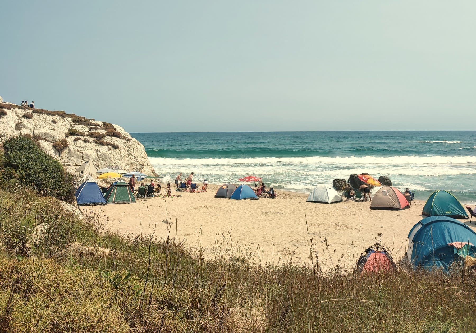 Dome tents pitched on the sand below a low white cliff, with surf breaking beyond them.